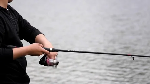 Slow motion of young man turning a fishing reel near lake Stock Footage 75876383
