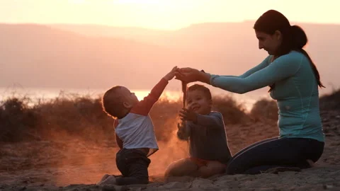 Slow motion of young mom playing with kids with sand at sunset. Video stock 149441248