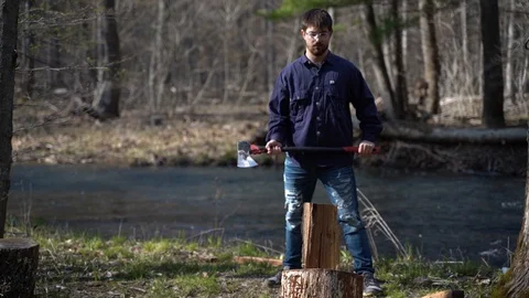 Slow motion of young stylish man splitting a log in the forest next to a flowing Stock Footage 129706367