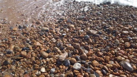 Slow motion zoom in on waves over pebbles on Brighton beach, England Video stock 115564940
