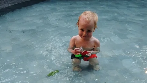 Slow motion.blonde boy of two years playing with a toy, sitting in the pool Stock Footage 104698620