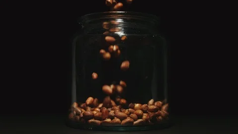 SLOW MOTION: Peeled peanuts falling into a glass jar Stock Footage 102889564