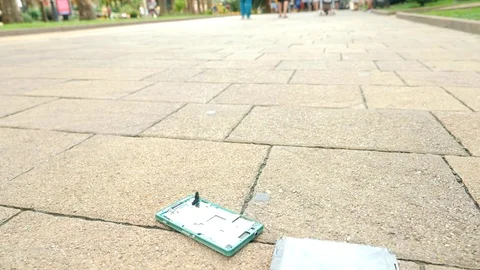 SLOW MOVEMENT: The smartphone falls on the asphalt on the street and splits into Stock Footage 79570230