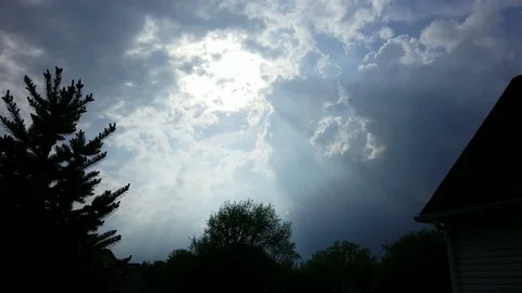 Slow-moving white clouds shift as the sun and sun rays appear Stock Footage 94132302