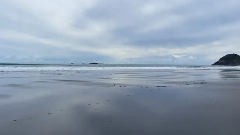 A slow pan across the black sand from the waves breaking towards the cliffs at B Stock Footage 208957936