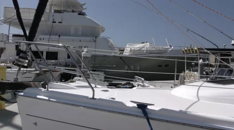 Slow pan across bow of docked sailing yachts with mega yacht in background. Stock Footage 67517502