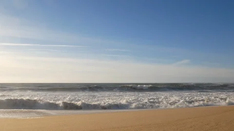 Slow pan down from blue sky with wispy clouds to waves breaking on a sandy beach Stock Footage 103288162