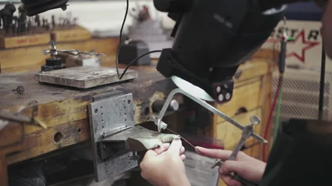 Slow pan down of a set of hands working on jewelry with a hacksaw blade Stock Footage 130671175