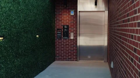 Slow pan of elevator entrance between hedge wall and brick corridor Stock Footage 332637397