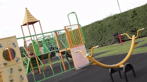 Slow panning shot of empty children's playground surrounded by a hedge Stock Footage 107627136