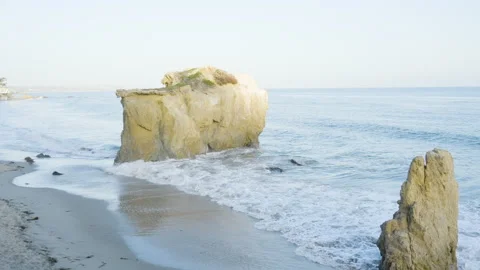 Slow panning shot of rolling waves crashing around large boulders located Stock Footage 220051603