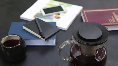 Slow panorama with teapot, cup, notebook, pen, cell phone and books around. Stock-Footage 76969521
