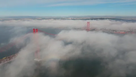 Slow panoramic drone shot of Lisbon's 25 de Abril Bridge emerging from dense Stock-Footage 348270254