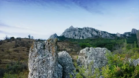 Slow panormanic flight past top of large stone against backdrop of mountainous Stock Footage 217406285