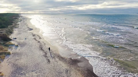 Slow pullback reveals solitary walker beside shimmering Baltic surf Stock Footage 340596591