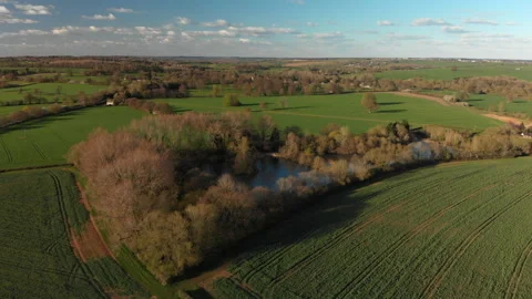 Slow reverse flight over fields and tree lined fishponds.  Spring Stock Footage