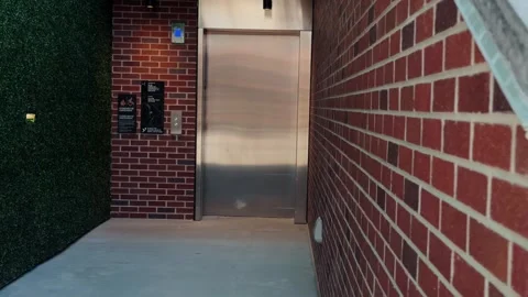 Slow right to left glide past elevator corridor with brick and hedge walls Stock Footage 332635933