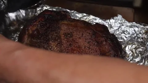 Slow-Smoked BBQ Pork Butt Wrapped in Aluminum Foil on a Rustic Surface Stock Footage 338212735