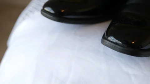 Slow tilt to close up of shiny black shoes sitting on bed 動画素材 100724941