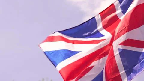 Slow tilt down past union jack waving in the wind with blue sky Video stock 240499807