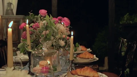 Slow tilt of festive table with serving, croissant, candles, macaroons, flowers. Video stock 76970744