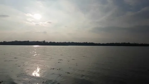 Slow tilt up showing waves on a river bank to then looking out over the river 動画素材 150116688