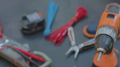 Slow tilt of tools - multimeter, knife, pliers, screw gun on black table. Video stock 76942174