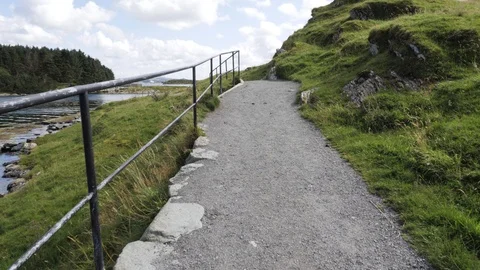 Slowly climb on narrow path along metal rails in hilly terrain near the river Stock Footage 88445514