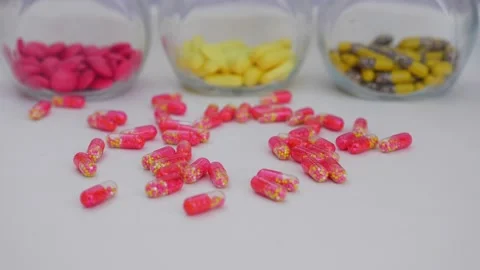 Slowly dropping capsules over a white table with colorful tablets in transpar Stock-Footage 147699663