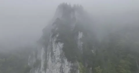 Slowly flying over a large rock cliff in thick fog in the wild Stock Footage 327383553