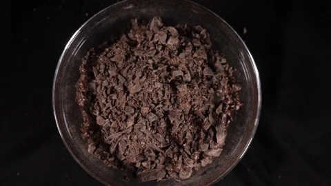 Slowly moving close-up dark pieces of chocolate falling into a glass bowl. Stock Footage 86567052