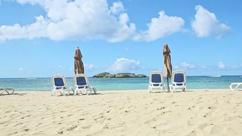 Slowly zoom in on empty ocean shore with long beach chairs and closed umbrellas Video stock 130030184