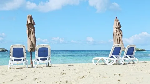 Slowly zoom out from empty sandy seashore with beach chairs and closed umbrellas Video stock 129779008