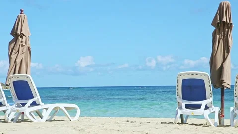 Slowly zoom out from empty sandy seashore with beach chairs and closed umbrellas Video stock 130483586