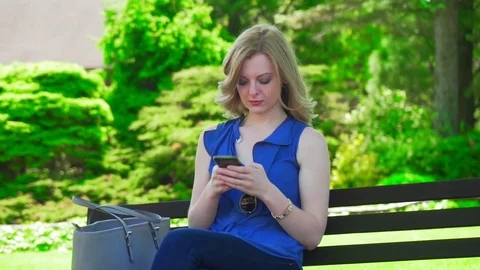 Slowmo blond women sitting using phone on park bench Vídeos de archivo 81768807