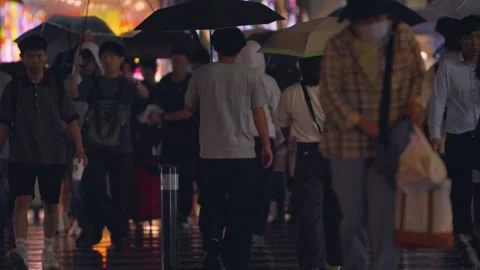 Slowmotion crowd walking under umbrellas across wet street at night Hakata Japan Stock Footage 331865144