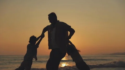 A slowmotion of a man spinning his two kids around against the sunset sky Stock Footage 122429253