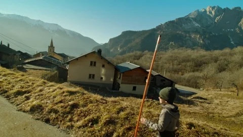 Slowmotion shot of boy running over grass hill trough french mountain village Stock Footage 71098717