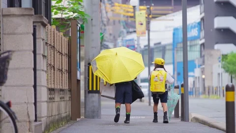 Slowmotion two school children walking with yellow umbrella and backpacks, rainy Stock Footage 322182071