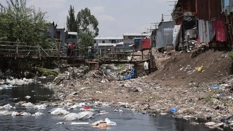Slum shacks by Ngong river, polluted with plastic waste and garbage, Nairobi Stock Footage 80244384