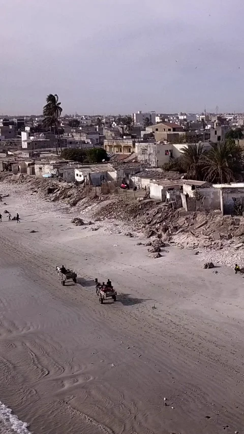 Slums built along sandy beach with horses passing, city buildings in background Video stock 230673013