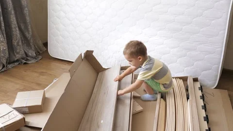 Small 2 years old blond caucasian boy is looking at the contents of the boxes Stock Footage 248349457