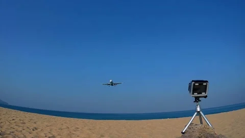 Small action camera on a tripod captures a plane flying low over a sandy beach Stock Footage 160811377