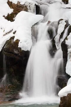 A small active waterfall. Clean mountain stream, snowy winter landscape Stock Photos