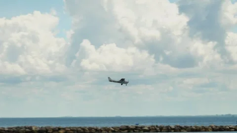 Small Airplane Flying Above a Tranquil Coastal Rock Barrier Jetty Under Cloudy S Stock Footage 314897588