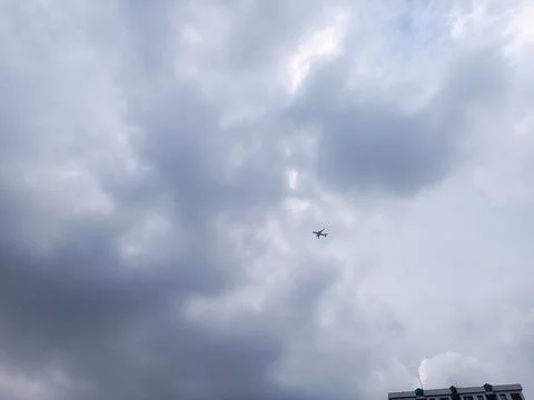 Small airplane flying through dark gray storm clouds over city buildings du.. Stock Photos