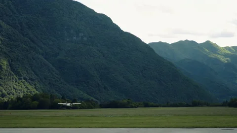Small airplane take off from the field, big green mountains in background. Stock Footage 132229643