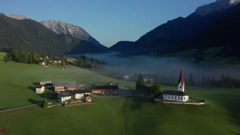 Small alpine mountain village with church covered in morning mist Vidéo 167962653
