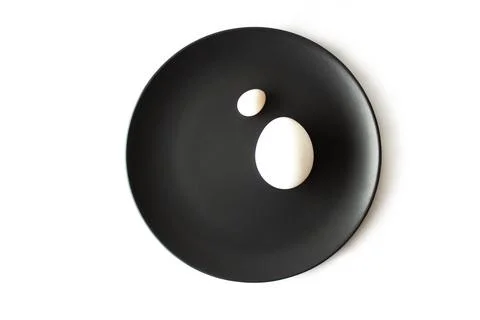 Small and large white egg on a black plate on an isolated white background Stock Photos