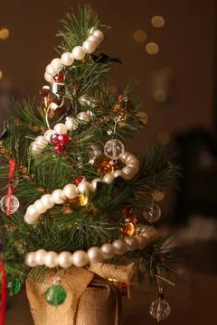 Small artificial Christmas tree decorated with beads and lights, set in a c.. Fotos Stock